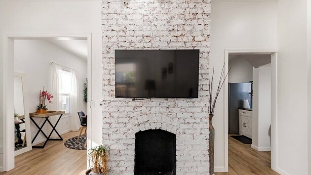 A living room with a white brick fireplace, a flat-screen TV mounted above it, and a dining area with a table and chairs.