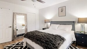 A bedroom with a bed, a ceiling fan, a nightstand, a lamp, a mirror, and a door.