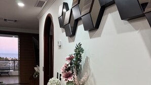 Un área de recepción con mostrador de madera, detalles decorativos en la pared, un jarrón con flores y vista al océano a través de un amplio ventanal.