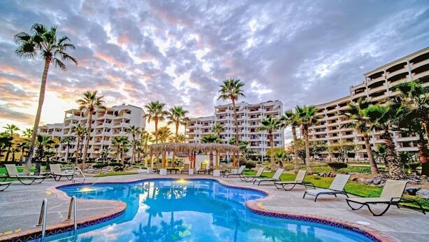 Un resort con una piscina grande, palmeras y edificios de varios pisos.