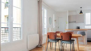 A modern kitchen with a wooden table and chairs, a window with a view of the street, and a radiator on the floor. - Blueground | Gros-Caillou, view, nr Eiffel Tower (Paris)
