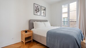 A bedroom with a bed, a nightstand, a window with a view, and two wall art pieces. - Blueground | Gros-Caillou, view, nr Eiffel Tower (Paris)