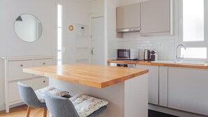 A modern kitchen with a wooden island, two grey chairs, a round mirror, and a black pendant light. - Blueground | Gros-Caillou, view, nr Eiffel Tower (Paris)