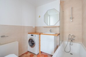 Une petite salle de bain équipée d’un lave-linge, d’un lavabo, d’un miroir et d’une baignoire.