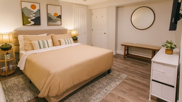 Une chambre à coucher avec un grand lit, des tables de chevet, un banc, un miroir et des œuvres d’art accrochées au mur.