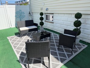 Une terrasse extérieure aménagée avec des meubles en osier, une table basse et des plantes ornementales taillées en forme.