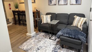 Un salon moderne avec un canapé gris, une petite table d’appoint, un tapis à motifs et des œuvres d’art abstraites accrochées au mur.