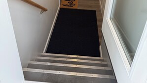 Un escalier étroit, avec un paillasson noir et une main courante en bois.