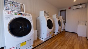 A row of front-loading washing machines in a laundry room with wooden flooring and white walls. - Hotel R9 The Yard Ube (Ube)