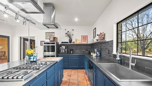 A modern kitchen with blue cabinets, a large island, a gas stove, and a window with a view of trees.