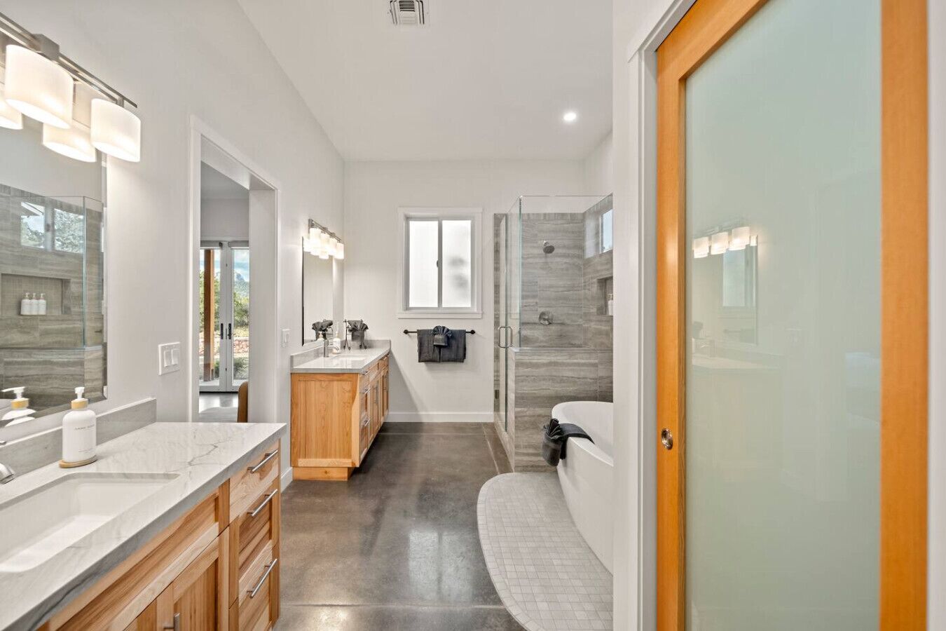 A modern bathroom with a large vanity, a shower, and a glass door leading to another room.