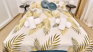 Una cama con colcha estampada con hojas, dos mesitas de noche con lámparas y una almohada azul.