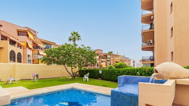 Una piscina con baldosas azules, rodeada de sillas de descanso y una palmera.