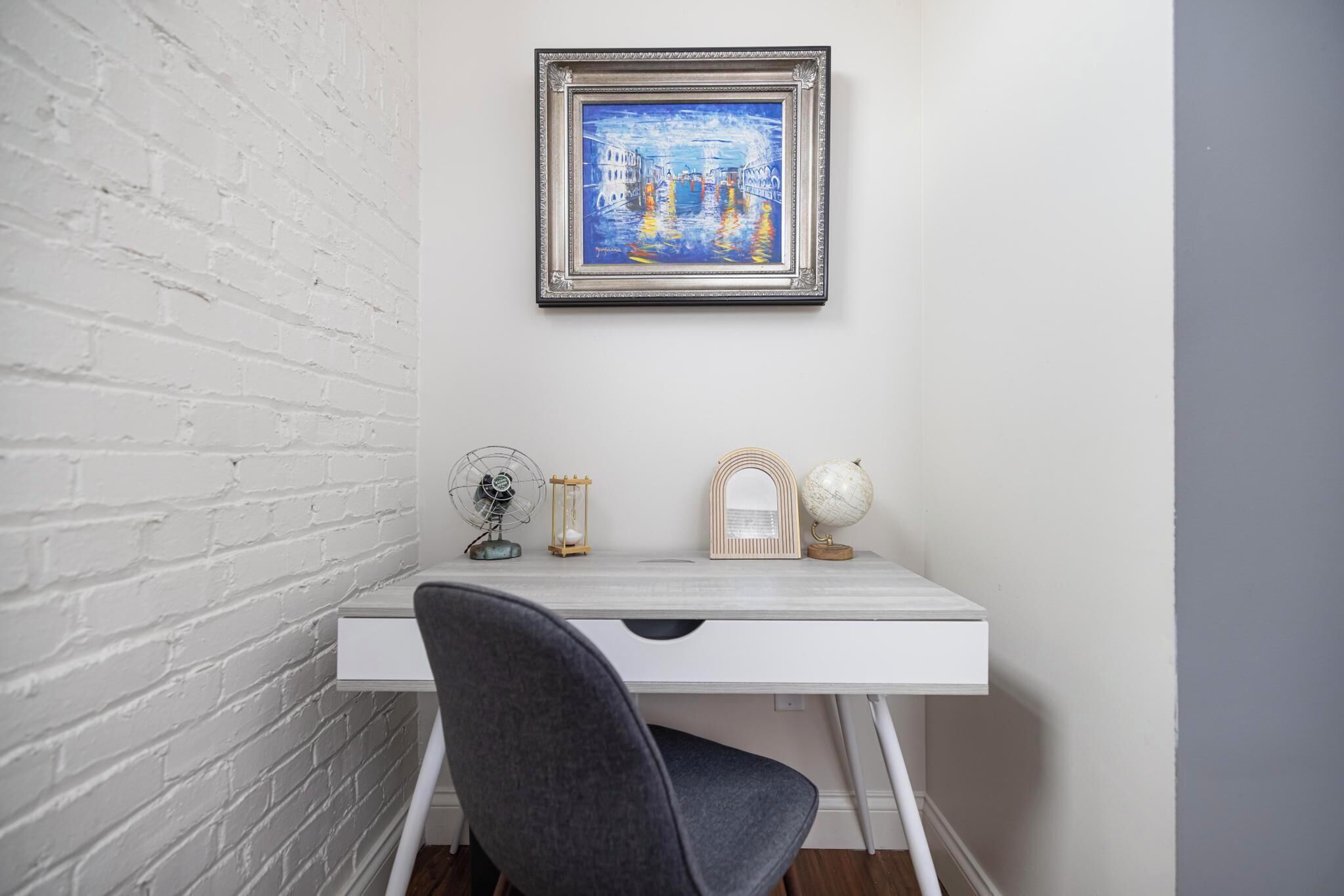 Un bureau blanc orné d’un tableau encadré, d’un globe terrestre et d’un ventilateur.