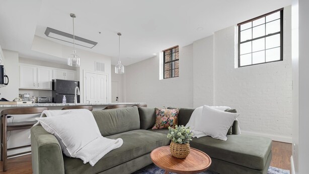 Ein modernes Wohnzimmer mit einem grünen Sofa, einem runden Holztisch und einer Küche im Hintergrund.