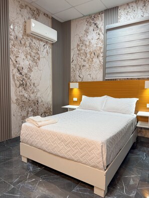 Une chambre à coucher moderne avec un mur à motifs de marbre, une tête de lit en bois, un lit doté d’un matelas matelassé et une table de chevet avec une lampe.