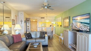 A modern living room with a leather sofa, a glass coffee table, and a television on a cabinet. - Sandpiper Key – Pool, Balcony & Beach Walks (Englewood)