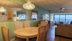 A dining area with a round table and wicker chairs, a sofa, and a television in the background. - Sandpiper Key – Pool, Balcony & Beach Walks (Englewood)