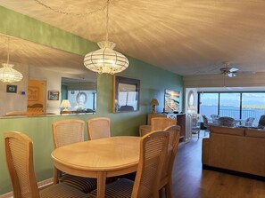 A dining area with a round table and wicker chairs, a sofa, and a television in the background. - Sandpiper Key – Pool, Balcony & Beach Walks (Englewood)
