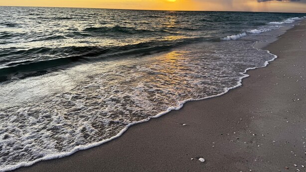 A beach with waves gently lapping onto the shore, a clear sky, and the sun setting on the horizon. - Sandpiper Key – Pool, Balcony & Beach Walks (Englewood)