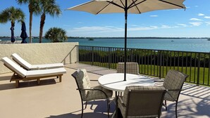 A balcony with a table and chairs, a lounge chair, and an umbrella. - Sandpiper Key – Pool, Balcony & Beach Walks (Englewood)
