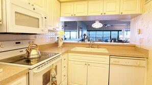 A kitchen with white cabinets, a microwave, stove, and dishwasher. There is a window with a view of the outside. - Sandpiper Key – Pool, Balcony & Beach Walks (Englewood)
