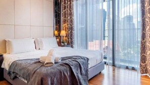 Habitación de hotel con cama, mesita de noche, lámpara y vistas amplias a través de grandes ventanales.