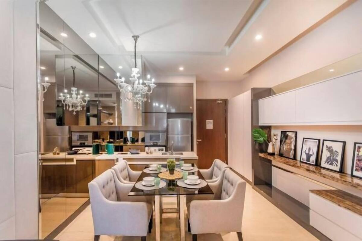 A modern dining area with a glass table, white upholstered chairs, and a chandelier.