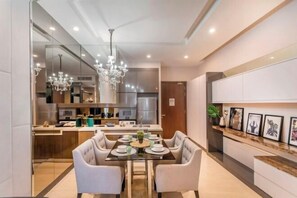 A modern dining area with a glass table, white upholstered chairs, and a chandelier. - Dorsett Bukit Bintang 5min to Pavilion KL (Kuala Lumpur)