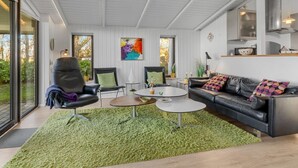 A modern living room with a black leather sofa, a round coffee table, and a green rug. There is a painting on the wall and a window with a view of trees. - "Sigbrit" - 100m from the sea by Interhome (Tranekær)