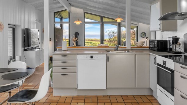 A modern kitchen with white cabinetry, a built-in oven, and a large window offering a view of the outdoors. - "Sigbrit" - 100m from the sea by Interhome (Tranekær)