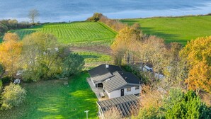 A house with a sloped roof, surrounded by green fields and trees, overlooking a large body of water. - "Sigbrit" - 100m from the sea by Interhome (Tranekær)