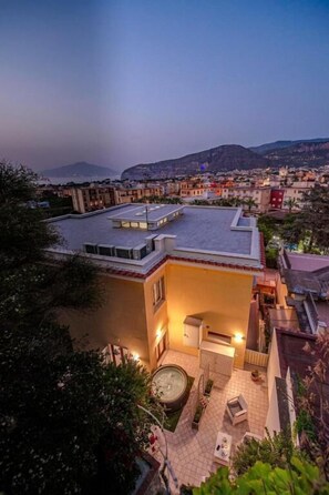 A modern building with a flat roof, a courtyard with a hot tub, and a view of the surrounding cityscape at dusk. - Casa Evelina (Sant'Agnello)