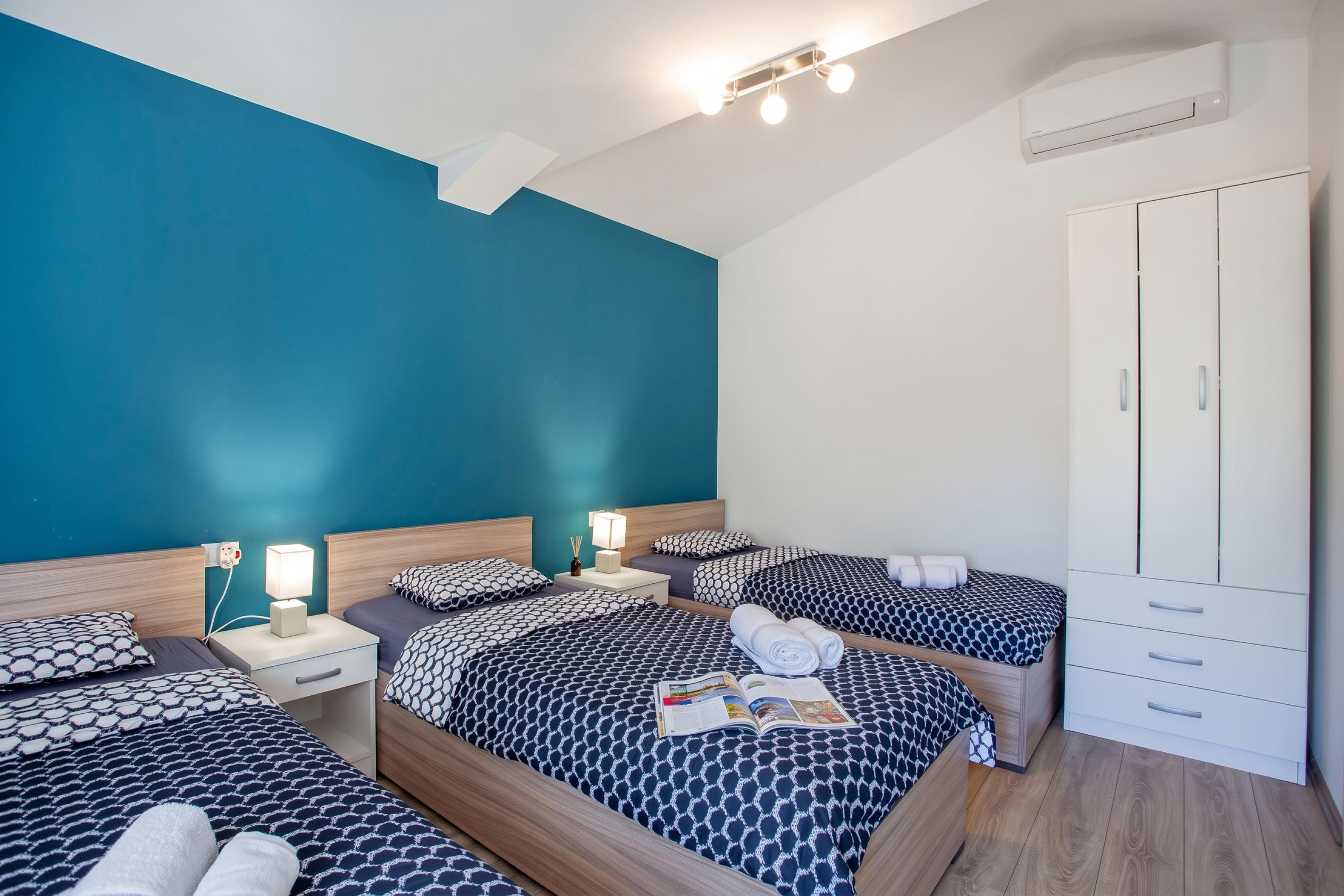 Habitación de hotel con pared de acento color turquesa, armario y varias camas con ropa de cama estampada.