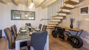 A dining area with a long table set for six, a modern chandelier, and a unique motorcycle-themed side table.