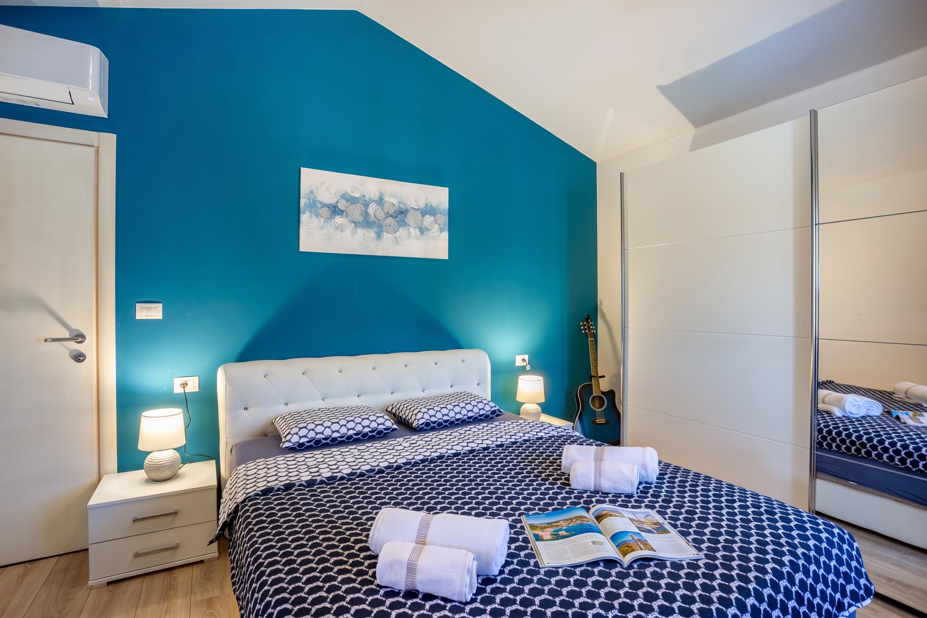 A bedroom with a bed, bedside lamps, a guitar, and a painting on the wall.