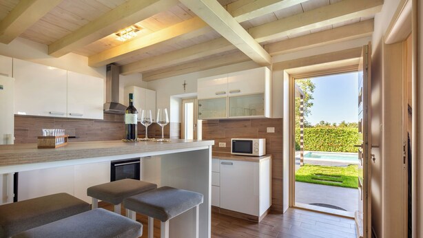 A modern kitchen with wooden beams, a bar area with stools, a microwave, and a view of a garden through an open door.