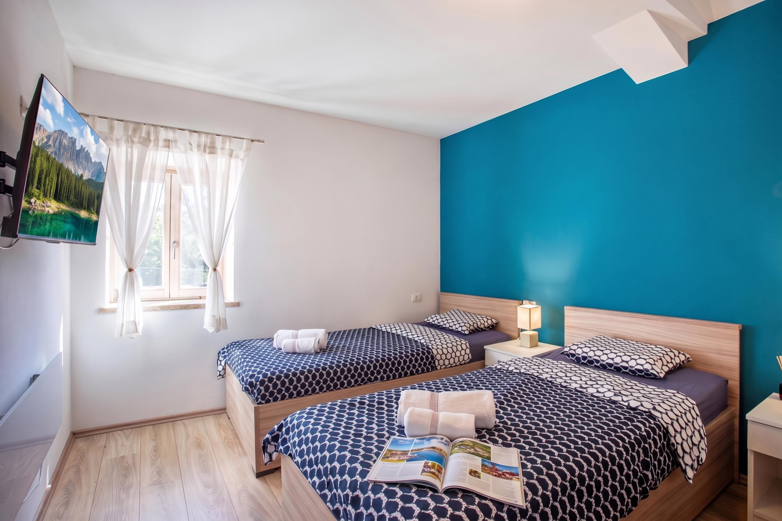 Une chambre d’hôtel avec deux lits, un téléviseur fixé au mur et une fenêtre avec des rideaux.