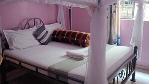 Un lit simple avec un baldaquin, des oreillers et une couverture, dans une pièce aux murs roses et dotée d’une fenêtre.