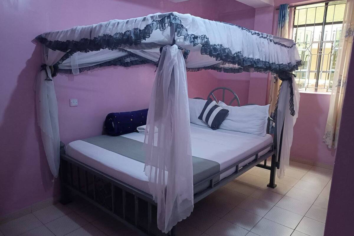 A single bed with a canopy, a bedside table, and a window with bars.