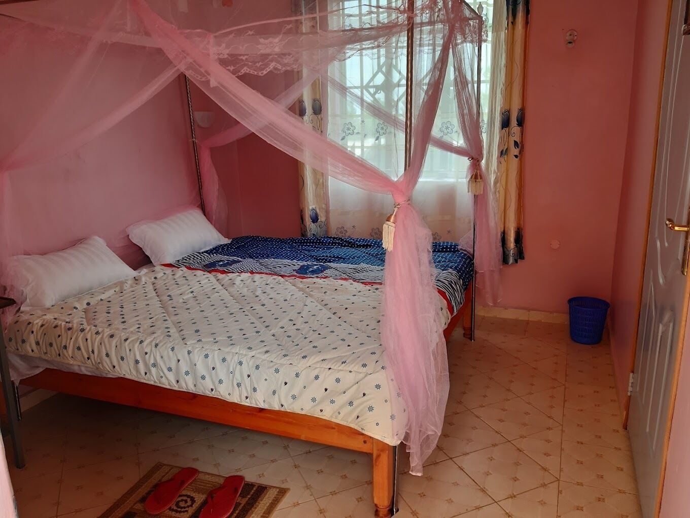 Un dormitorio con cama, mosquitero, ventana con cortinas y una cesta azul.