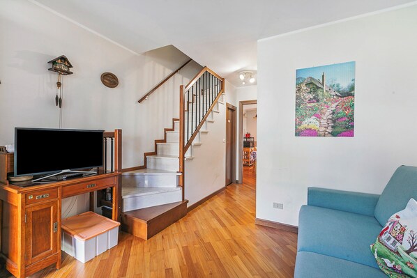 A living room with a wooden TV stand, a blue sofa, a staircase, and a wall-mounted picture.