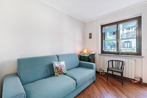 A room with a blue sofa, a wooden chair, a radiator, and a window with a view of buildings.