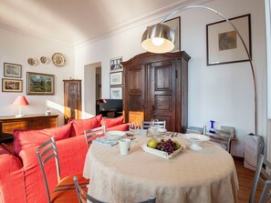 A dining area with a round table set for four, surrounded by red upholstered chairs. A large wooden cabinet is in the background, and the room has white walls with framed pictures.