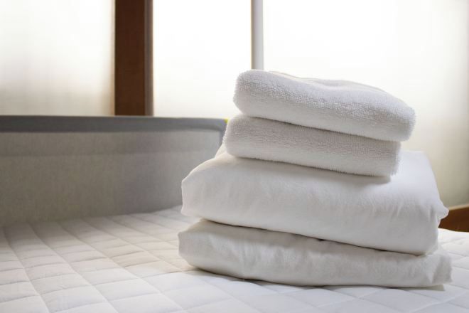 A stack of white towels on a bed with a quilted cover.