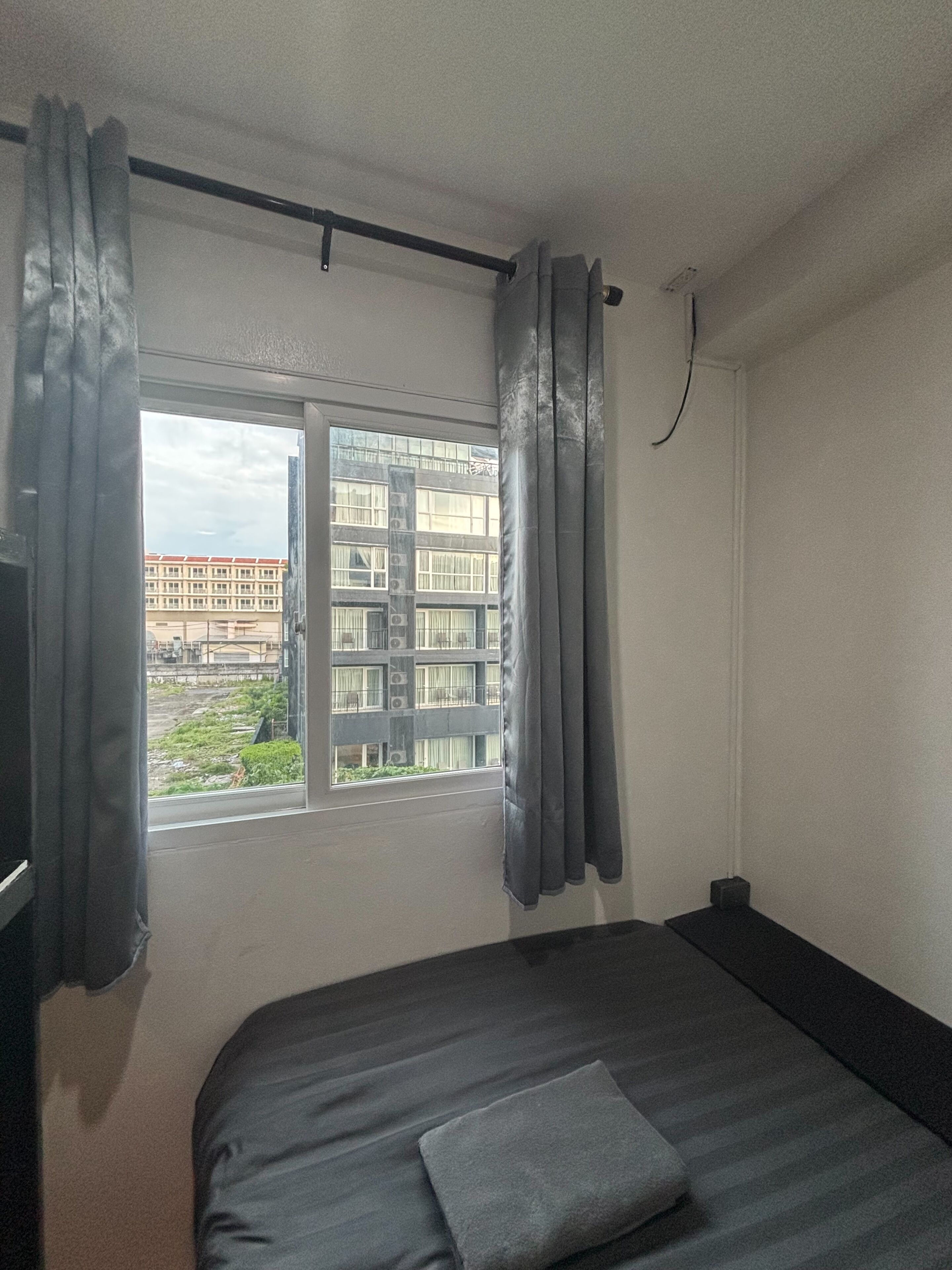 Une chambre à coucher avec un lit, une fenêtre avec des rideaux et une vue sur les bâtiments à l’extérieur.