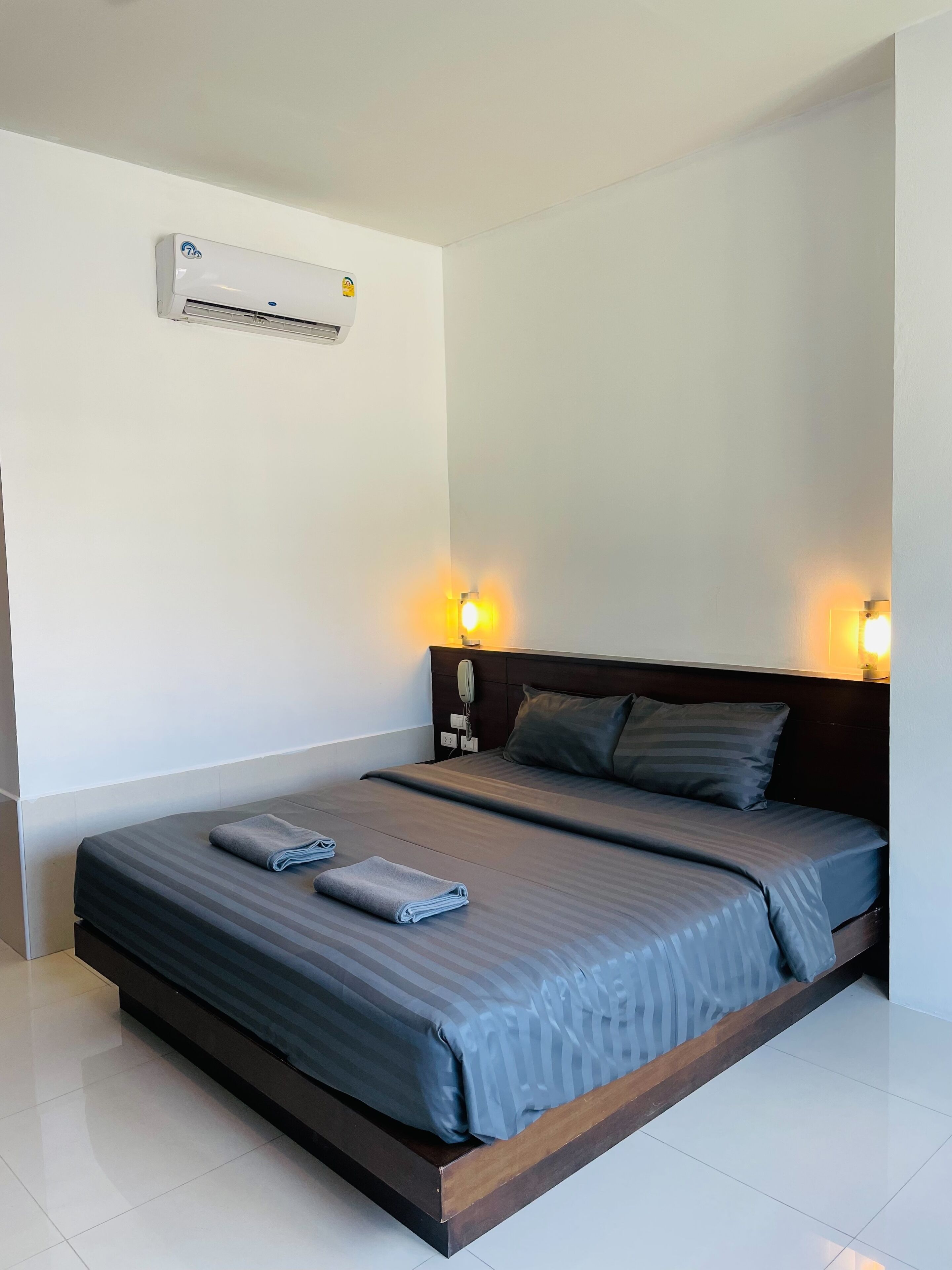 A hotel room with a bed, a wall-mounted air conditioner, and bedside lamps.