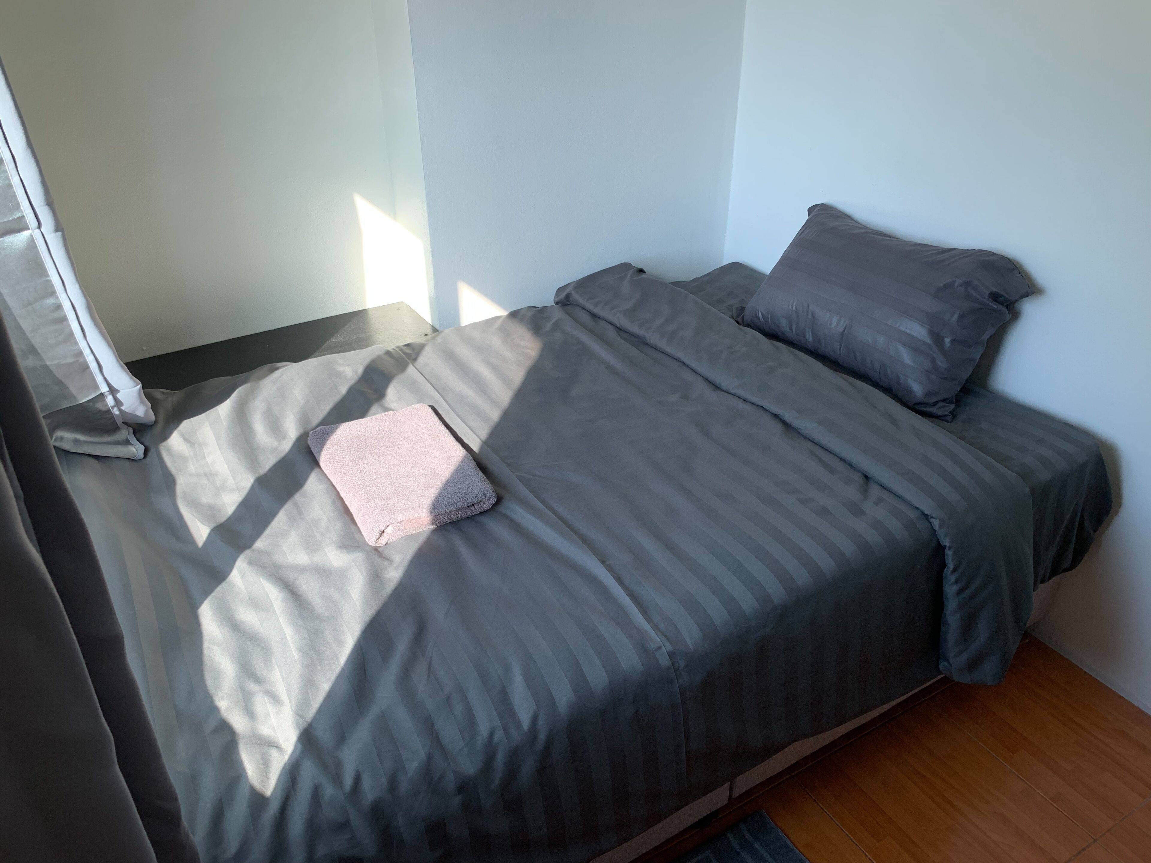 A single bed with grey bedding, a pink pillow, and a wooden floor.