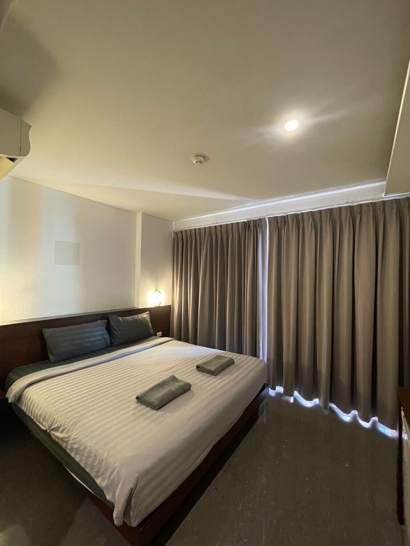A hotel room with a large bed, a headboard, a wall-mounted light, and a window with curtains.