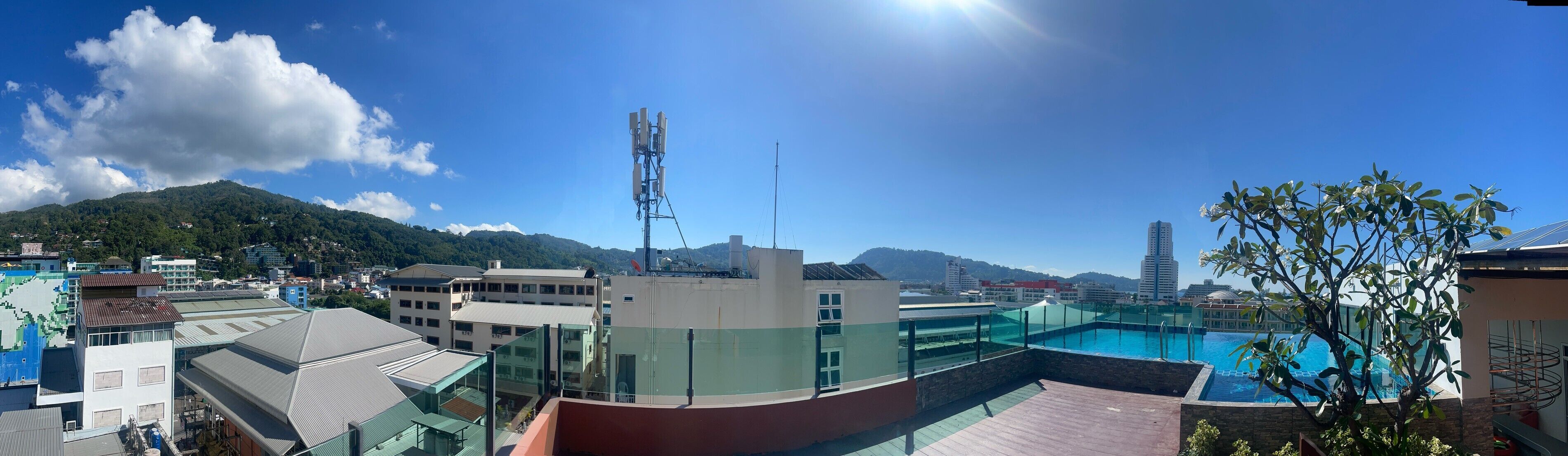 Un edificio moderno con piscina en la azotea, rodeado de edificios urbanos y montañas al fondo.